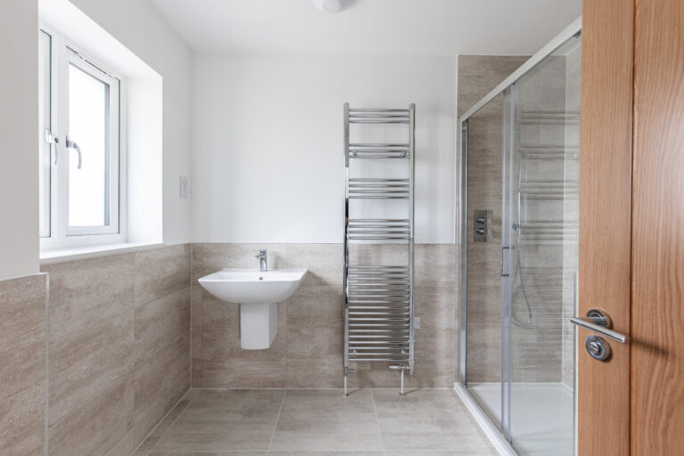 Ensuite bathroom with double shower cubicle, large glass shower screen, full height chrome towel rail, half height tiling and floating sink.