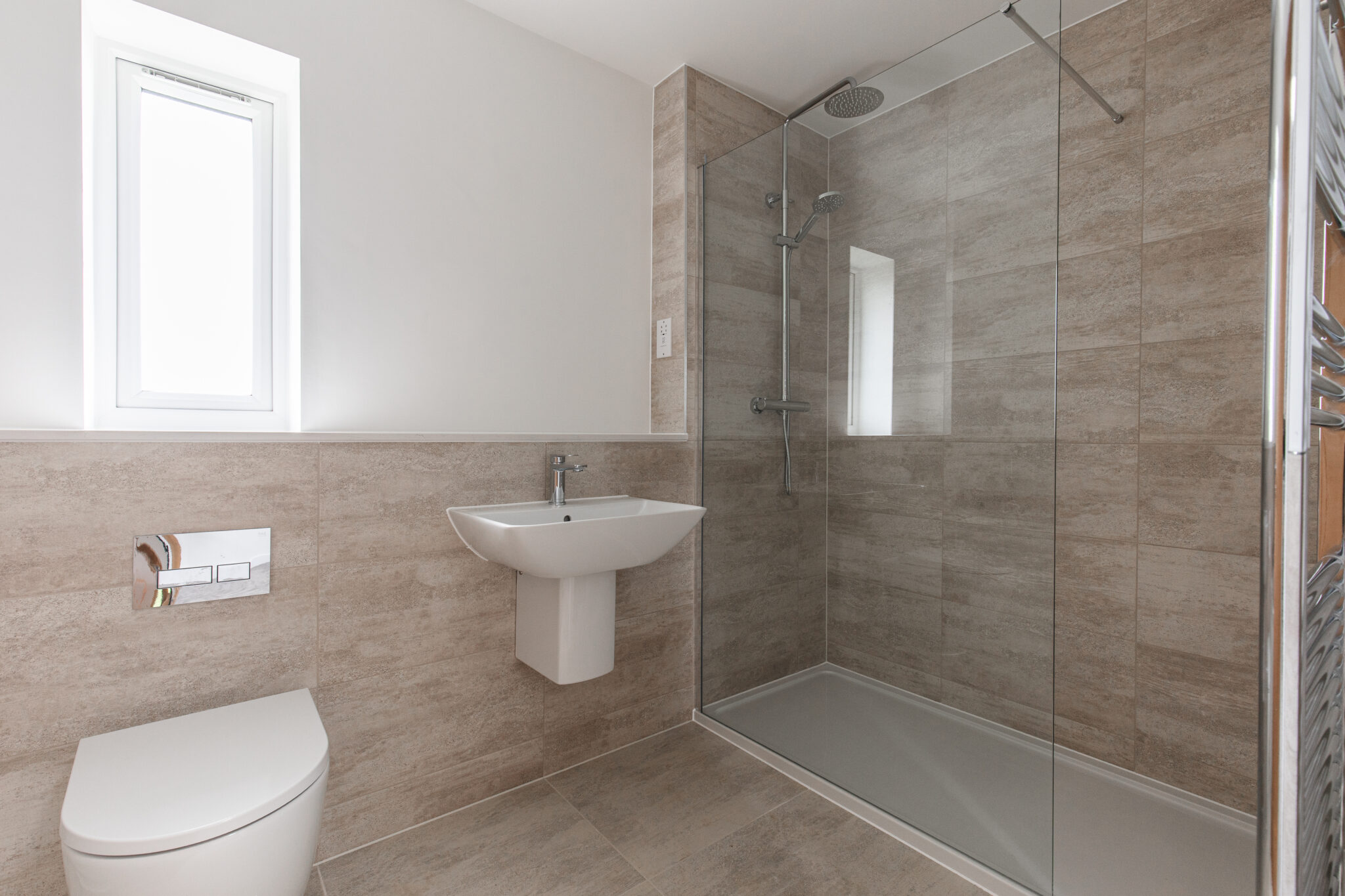 Ensuite bathroom with double shower cubicle, large glass shower screen, floating sink and half height taupe tiles.